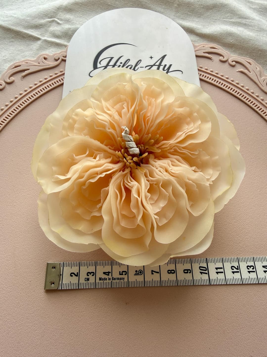 A Juliet rose candle held beside a measuring tape, showing that the bloom is about the width of a hand